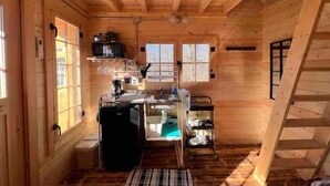 A compact wooden cabin with a kitchenette, a small sink, and a window. - Après Vine Tiny Cabin at Panther's Rest Farm (Makanda)
