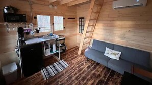 Een compact vakantiehuisje met een kitchenette, een slaapbank en een ladder naar een slaapzolder.