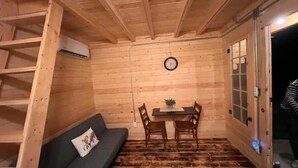 A wooden interior with a sofa, a small table with chairs, and a clock on the wall. - Après Vine Tiny Cabin at Panther's Rest Farm (Makanda)