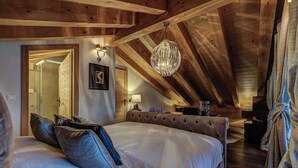 A bedroom with a large bed, wooden ceiling beams, a chandelier, and a framed picture on the wall. - Stunning Chalet Adele on the Piste (Veysonnaz)