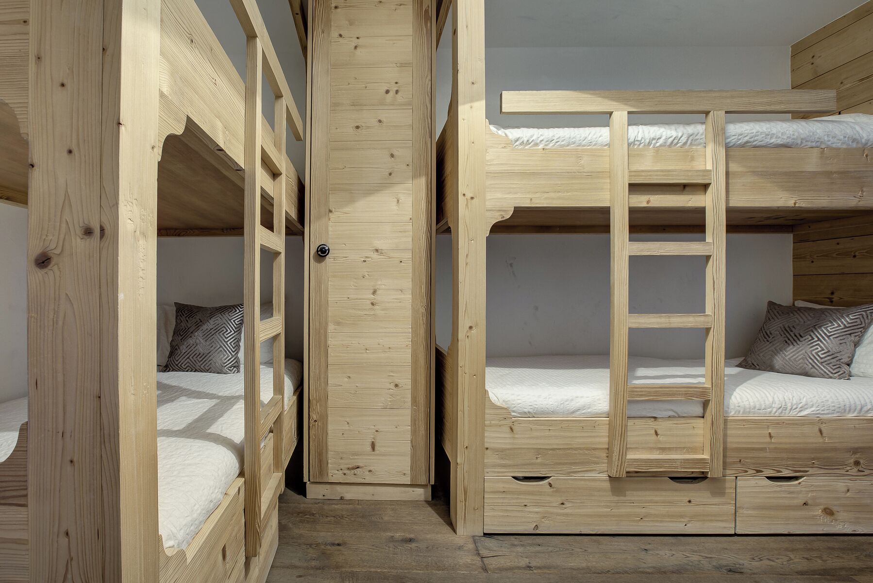 A bunk bed room with wooden walls and floors, a ladder, and patterned pillows.