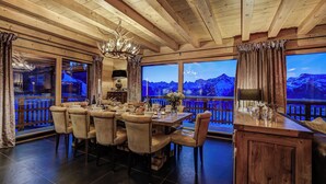 A dining area with a wooden ceiling, large windows with a mountain view, and a chandelier. - Stunning Chalet Adele on the Piste (Veysonnaz)