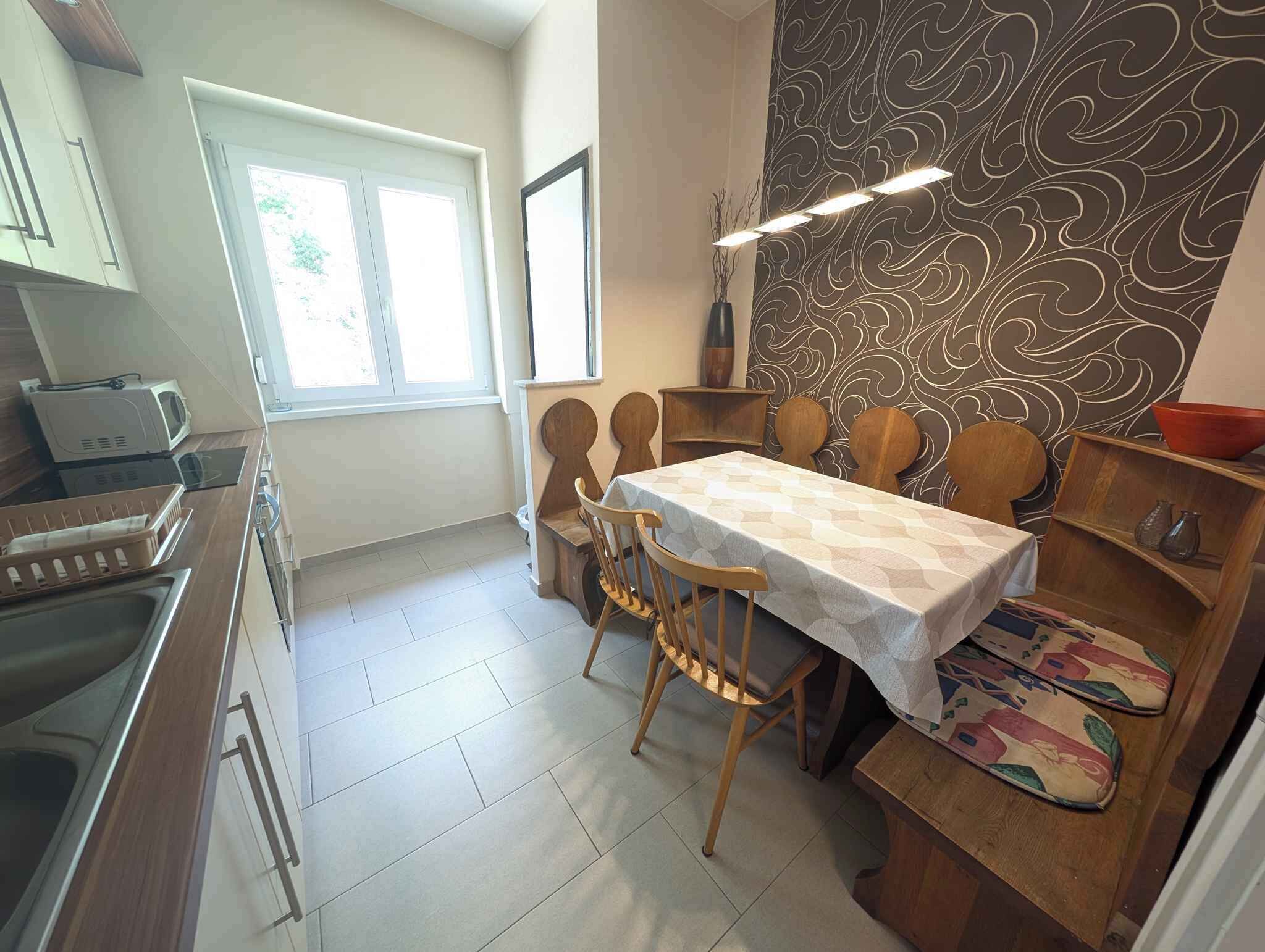 A compact kitchen with a dining area, featuring a microwave, sink, and wooden chairs.