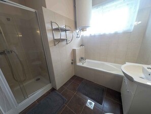 Een badkamer met een douchecabine van glas, een bad, een wastafel en een raam met gordijnen.