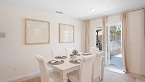 A dining area with a white table set for six, two framed abstract artworks on the wall, and a sliding glass door leading to an outdoor area. - Serenity, a tranquil 4-bed, 3-bath home minutes away from UC Merced.  (Merced)