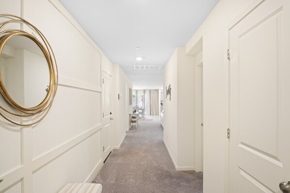 A hallway with white walls, a carpeted floor, and a large mirror on the left. - Serenity, a tranquil 4-bed, 3-bath home minutes away from UC Merced. (Merced)