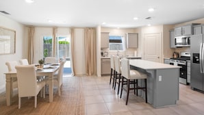 A modern kitchen with a central island, built-in appliances, and a dining area with a table and chairs. - Serenity, a tranquil 4-bed, 3-bath home minutes away from UC Merced.  (Merced)