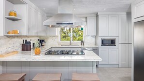 Cocina moderna con armarios blancos, una isla central con taburetes, estufa a gas y microondas.