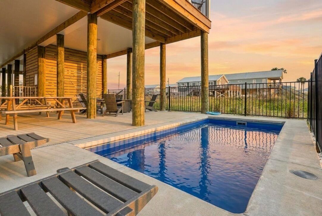 Piscina com deck de madeira e espreguiçadeiras, cercada por uma grade.