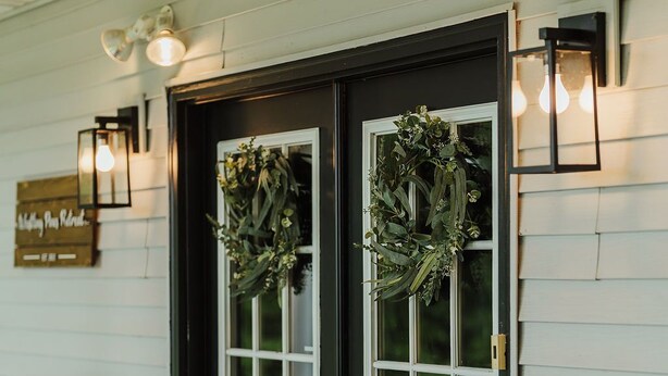 A porch with two black-framed glass doors, a bench, and a sign that reads "Welcome Play Retreat."