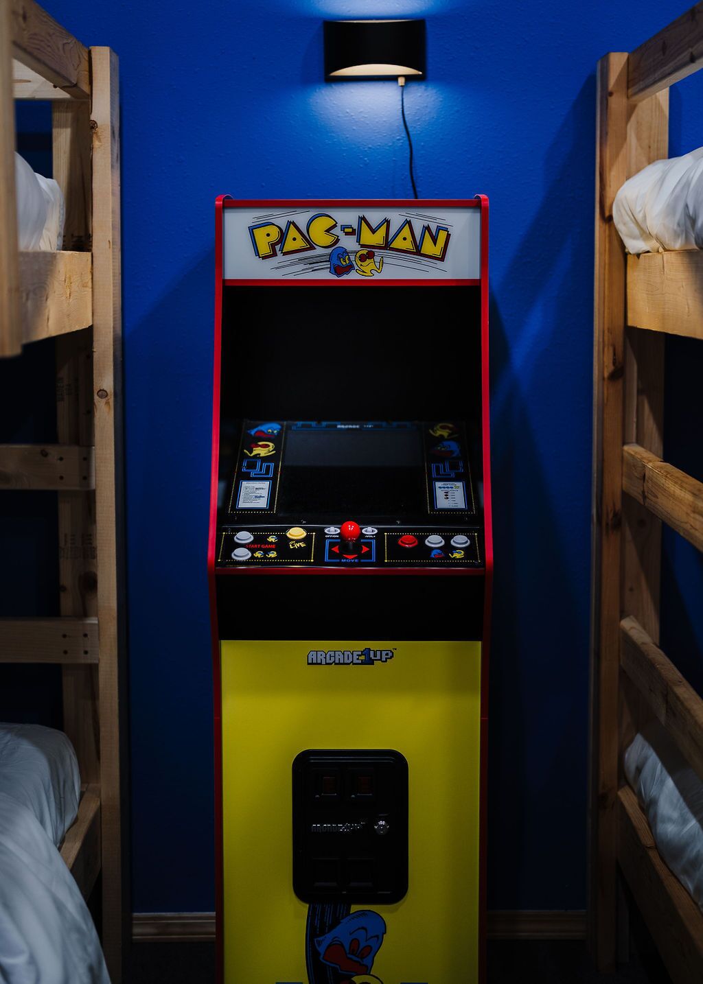 Ein Pac-Man-Automatenraum mit blauen Wänden und Holzbettkästen.