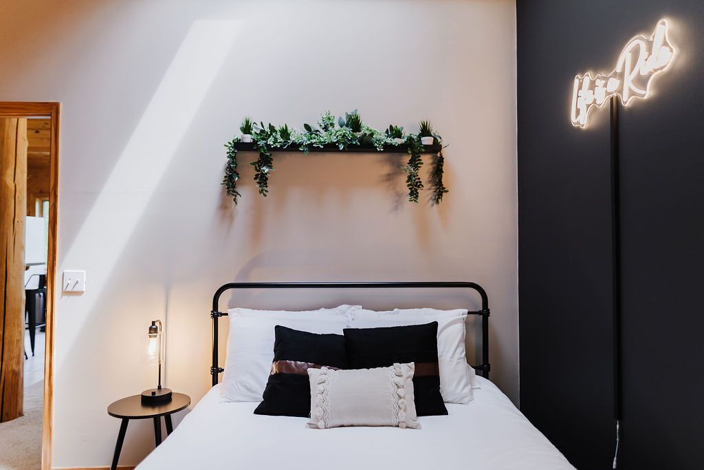 Camera da letto con un letto, comodino, mensola a muro con piante e insegna luminosa al neon.
