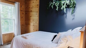 A neatly made bed with white linens in a room with wooden walls and a dark accent wall.