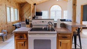 A kitchen with wooden walls, a stove, a kettle, and a sink.