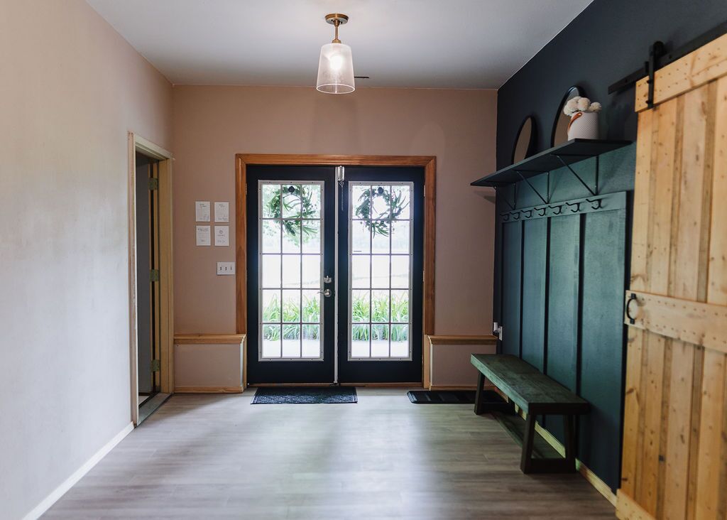 A hallway with a wooden bench, a door with a wreath, and a light fixture.