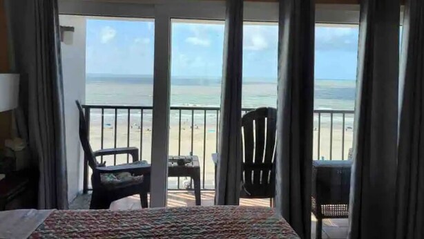 Een hotelkamer met een balkon met uitzicht op een strand.