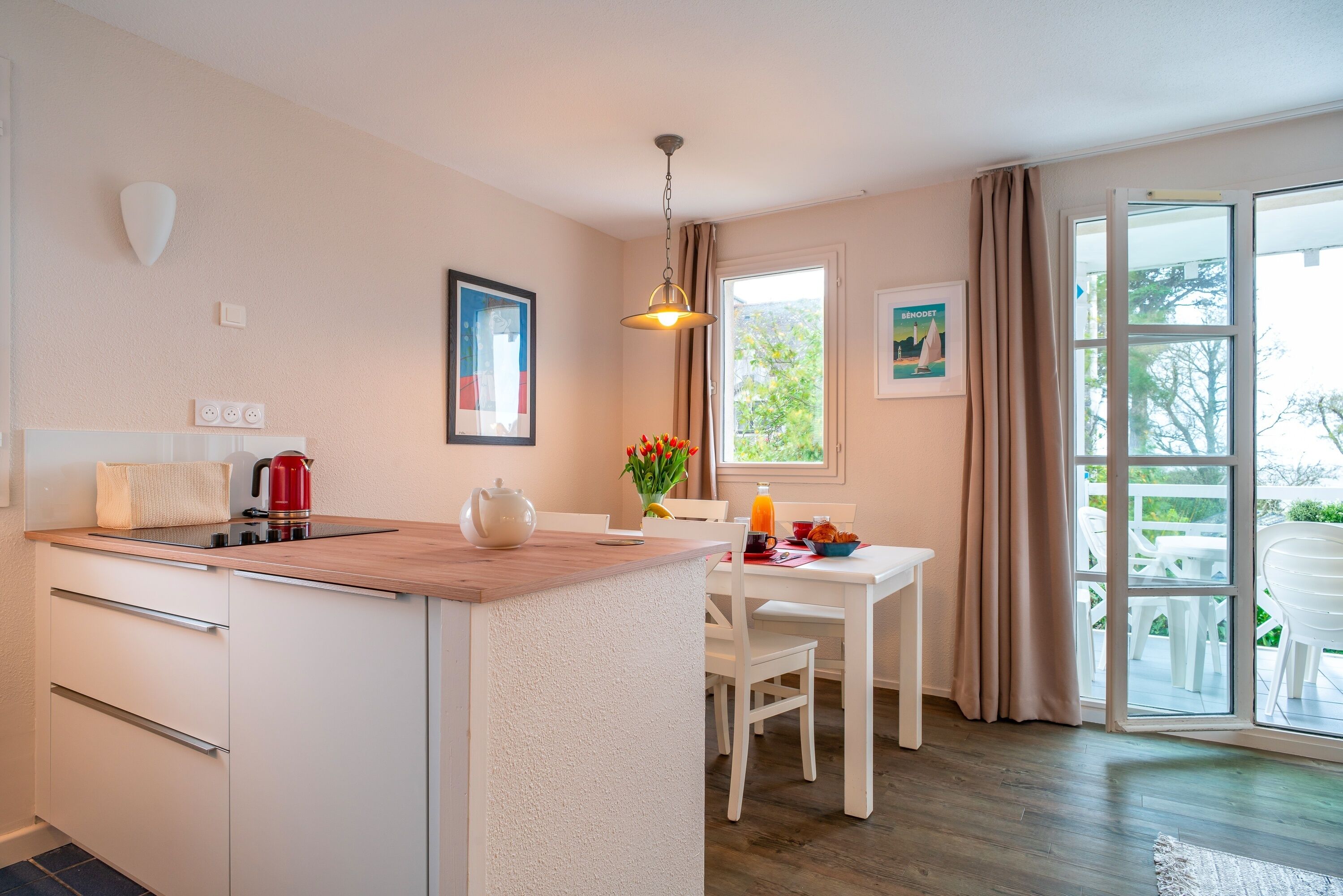 Una cocina moderna con encimera de madera, armarios blancos y un área de comedor con mesa y sillas blancas.