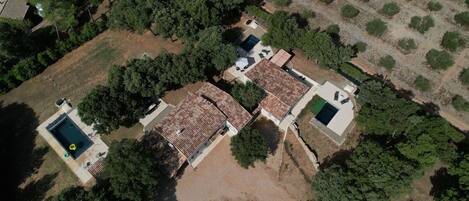 Vista aérea de una zona residencial con tres casas, cada una con tejado de tejas, rodeadas de árboles y jardines.
