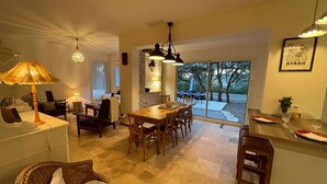 A dining area with a table and chairs, a wicker chair, a lamp, and a view of the outdoors through large sliding doors. - Coeur de Lavande - Maison climatisée avec piscine (Fox-Amphoux)