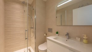 Un baño moderno con ducha de vidrio, un lavamanos blanco y un espejo sobre el lavamanos.