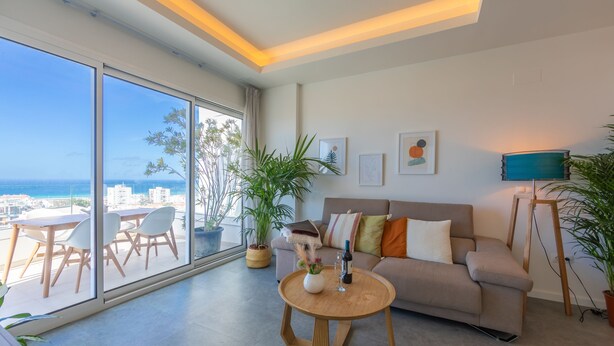 Una sala de estar moderna con un ventanal grande, un sofá, una mesa de centro y plantas en macetas.