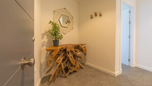 Un pasillo con una consola de madera, una planta en maceta y un espejo geométrico en la pared.