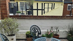 A wooden deck with a round metal table and two chairs, surrounded by potted plants.