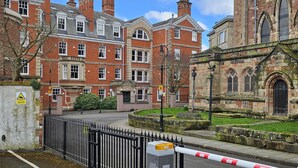 A gated entrance to a historic building with red brick architecture and a large arched window.