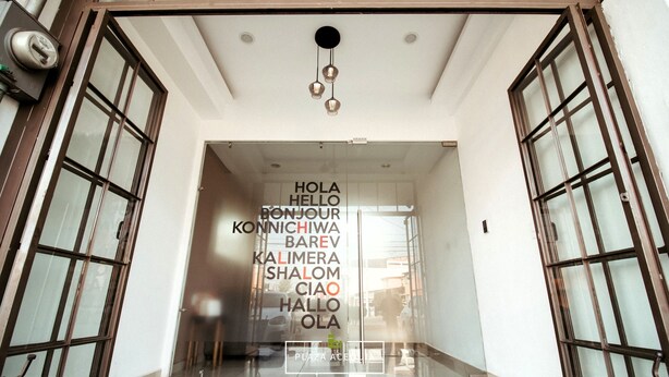 Entrada de hotel con puerta de cristal y cartel de bienvenida en varios idiomas.