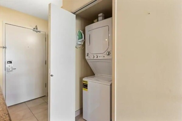 Uma lavanderia com máquina de lavar e secadora, uma porta com fechadura e piso ladrilhado.