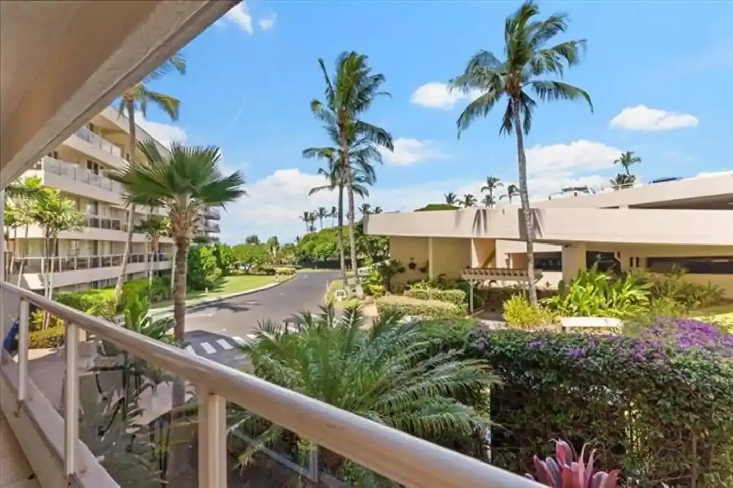 A balcony with a view of a road, palm trees, and a building with a flat roof.