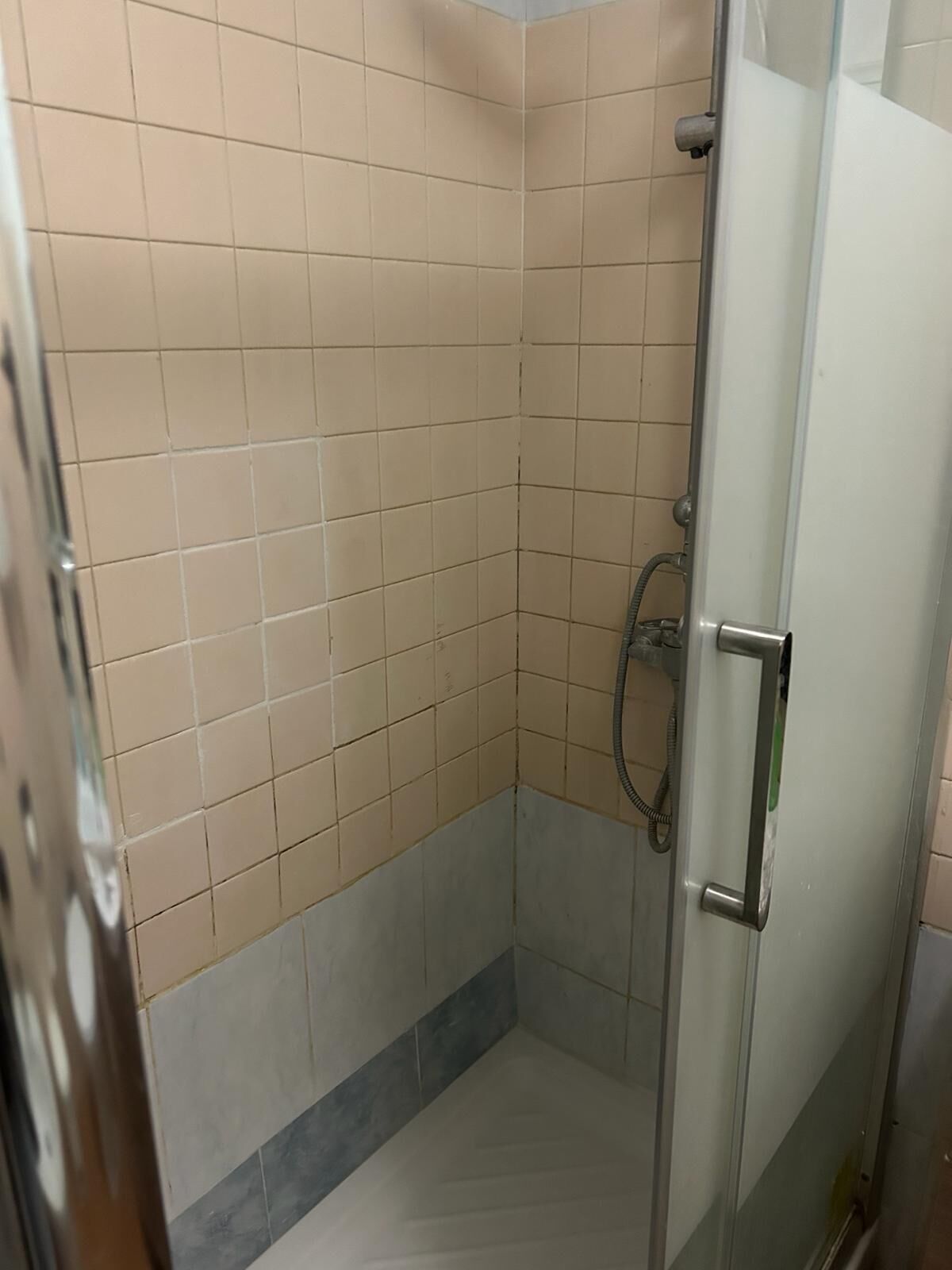 A small, tiled shower room with a glass door and a metal handle.
