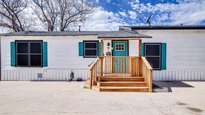 A single-story house with a wooden front porch, a green door, and a satellite dish on the roof.