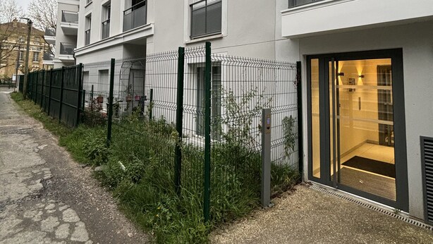A modern apartment building with balconies, a gated entrance, and a pathway leading to the entrance.