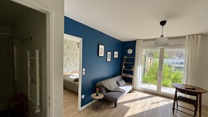 A room with a blue accent wall, a gray sofa, a wooden floor, a small round table, and a view of greenery outside.