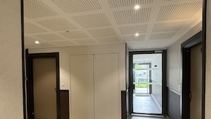 A hallway with a tiled floor, a ceiling with a grid pattern, and a door leading to a balcony.
