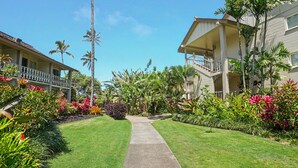 A pathway leading to a building with a balcony, surrounded by lush tropical plants and palm trees. - New from Premier Host -  Top Floor Oceanview Studio at Islander on the Beach (Kapaʻa)