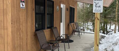 A wooden building with two signs warning of moose. There are four chairs outside.