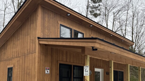 Una baita di legno con un portico, due finestre e una porta.
