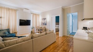 Ein modernes Wohnzimmer mit einem beigefarbenen Sofa, einem Fernseher und einem Essbereich mit Tisch und Stühlen.