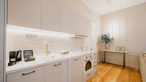 Eine moderne Küche mit weißen Schränken, einem eingebauten Backofen und einer Arbeitsplatte mit Wasserkocher und kleiner Pflanze.