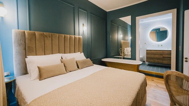 Ein Schlafzimmer mit einem großen Bett, einem Nachttisch, einem Sessel, einem Schminktisch mit Spiegel und einer Badewanne.