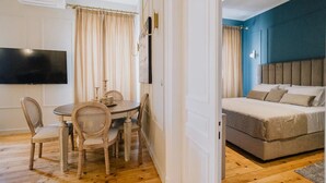 Ein Zimmer mit einem Bett, einem Fernseher, einem Esstisch mit Stühlen und einer blauen Akzentwand.