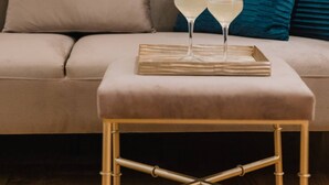 Un salon moderne avec un canapé beige, des coussins turquoise et une petite table basse en bois sur laquelle reposent deux verres de vin blanc.