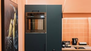 A compact living space with a sofa, a small round table, a kitchen area with a stove, and a tiled backsplash. - Mantzarou #6 - Corfu Town Luxury Suites

 (Kerkira)