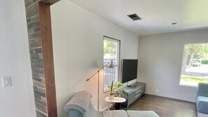 Un salon moderne avec un canapé d’angle, une petite table d’appoint avec une lampe, un téléviseur et une fenêtre donnant sur l’extérieur.