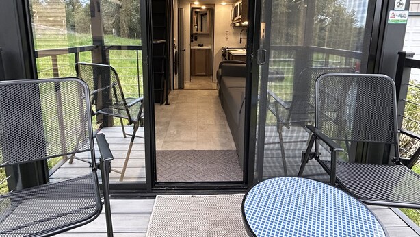A modern outdoor seating area with metal chairs and a round table, leading to a kitchen and a balcony with a view of the outdoors. - New tiny house near Grass Valley - hot tub access! (Rough and Ready)