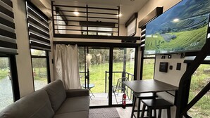 A modern interior with a sofa, a small table, a TV displaying a landscape, and a door leading to an outdoor area. - New tiny house near Grass Valley - hot tub access! (Rough and Ready)