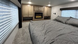 A bedroom with a bed, a fireplace, wooden cabinets, and a window with blinds. - New tiny house near Grass Valley - hot tub access! (Rough and Ready)