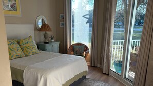 Une chambre à coucher avec un grand lit, une table de chevet, une lampe et une vue sur l’extérieur grâce à une porte-fenêtre coulissante.